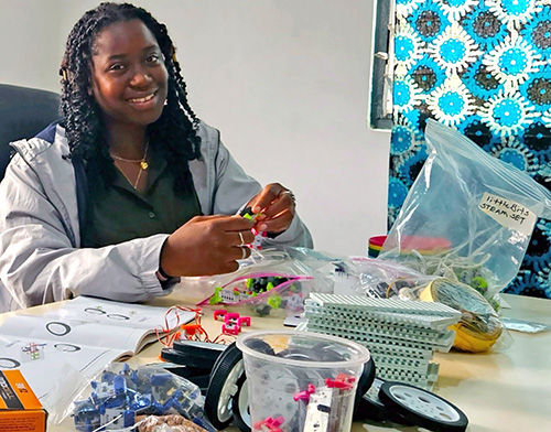 A student smiles while working with a variety of pieces, an instruction manual open to her right.