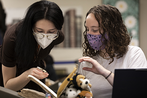 Two people wearing a mask open a book.