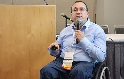 A speaker in a wheelchair talks into a handheld microphone.