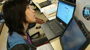 A woman uses a computer at the same time as assistive technology