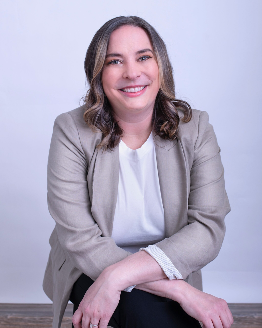 Kate Sonka sits with arms crossed over her lap while smiling for the camera