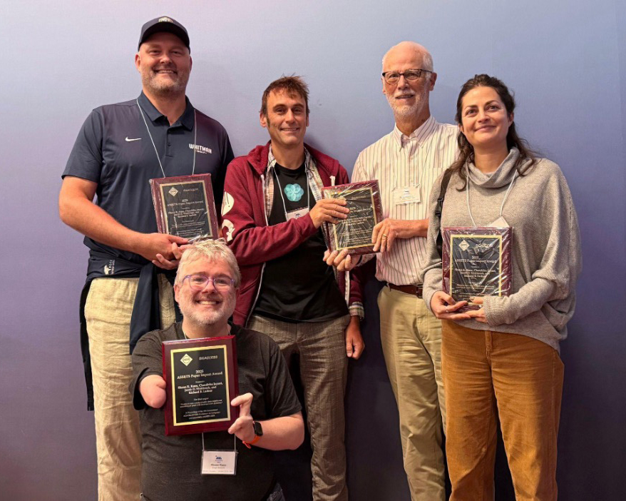 The four authors hold their awards and pose with the chair of the committee.