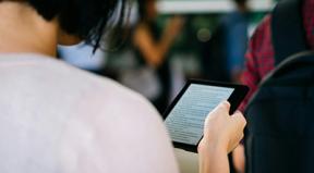 A person holding up a tablet and reading while in a bustling room