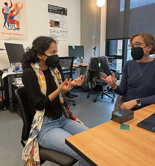 Two academics sign to each other while surrounded by computers and equipment.