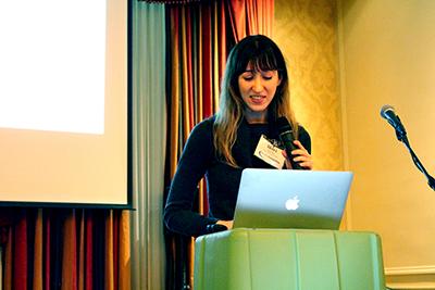 A partner uses a laptop while holding a mic at a podium.