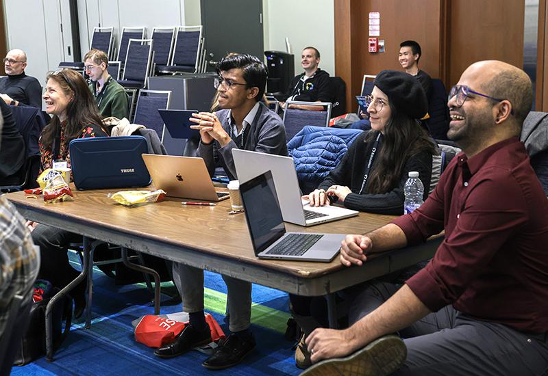 Educators sit around a table with laptops out, smiling and laughing